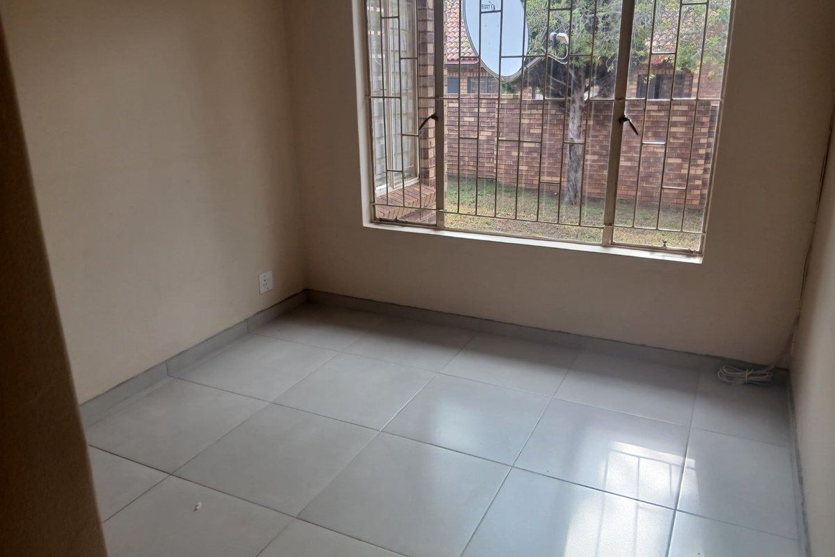 A vacant bedroom featuring neutral tiled flooring and a large window fitted with security bars, offering a clean and blank canvas.