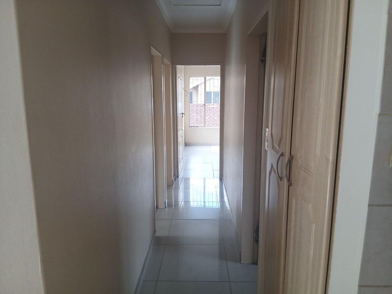 A clean, tiled hallway featuring built-in storage cupboards and access to adjacent rooms, leading towards a windowed area at the end.