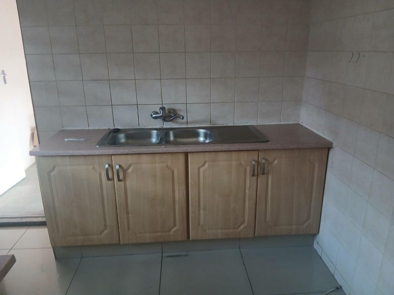 A functional kitchen area featuring a double bowl stainless steel sink, laminate countertop, and built-in base cabinetry with tiled walls and flooring.