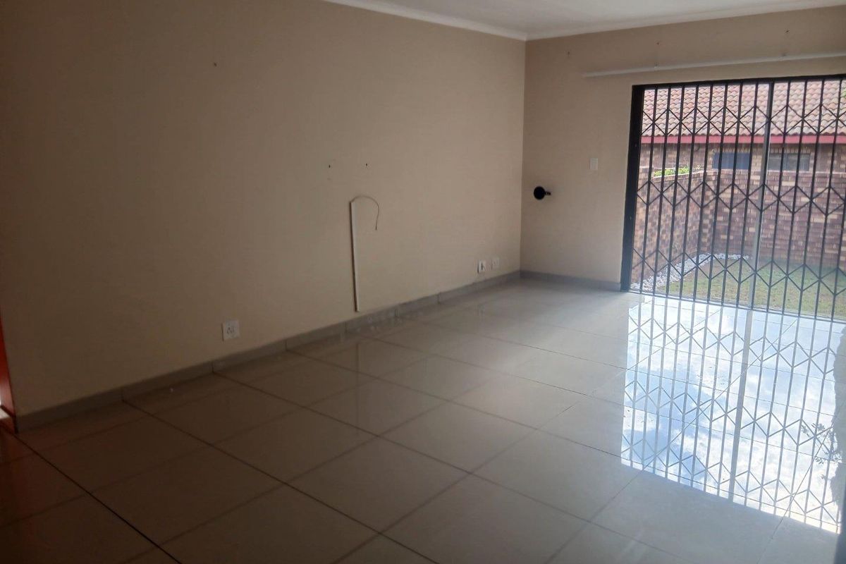 An empty living room featuring neutral tiled flooring and a sliding glass door with a security gate leading to the exterior.