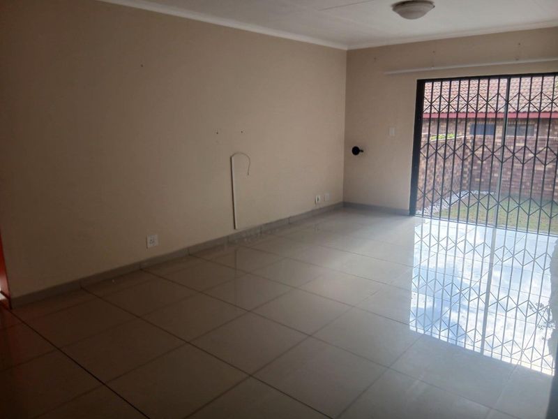 An empty living room featuring neutral tiled flooring and a sliding glass door with a security gate leading to the exterior.