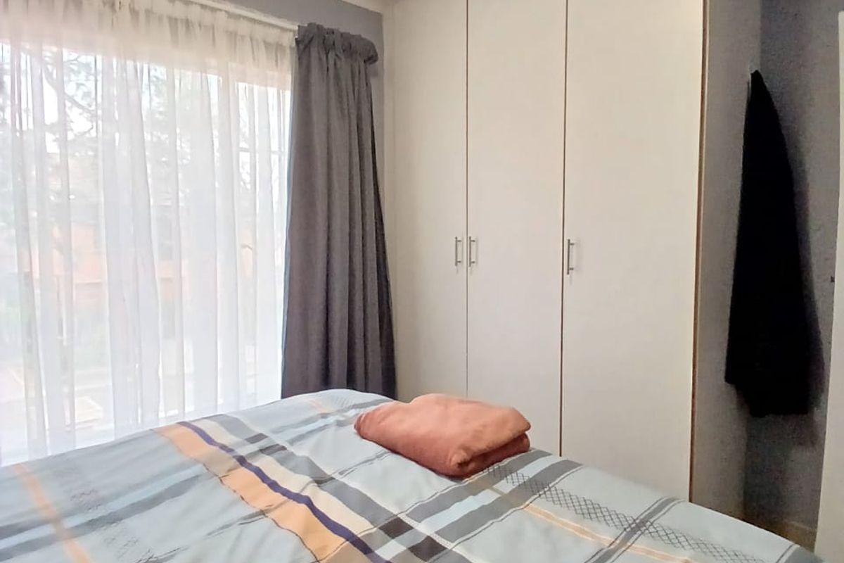 A bedroom featuring built-in cupboards and large windows with curtain tracks, providing natural light and storage space.