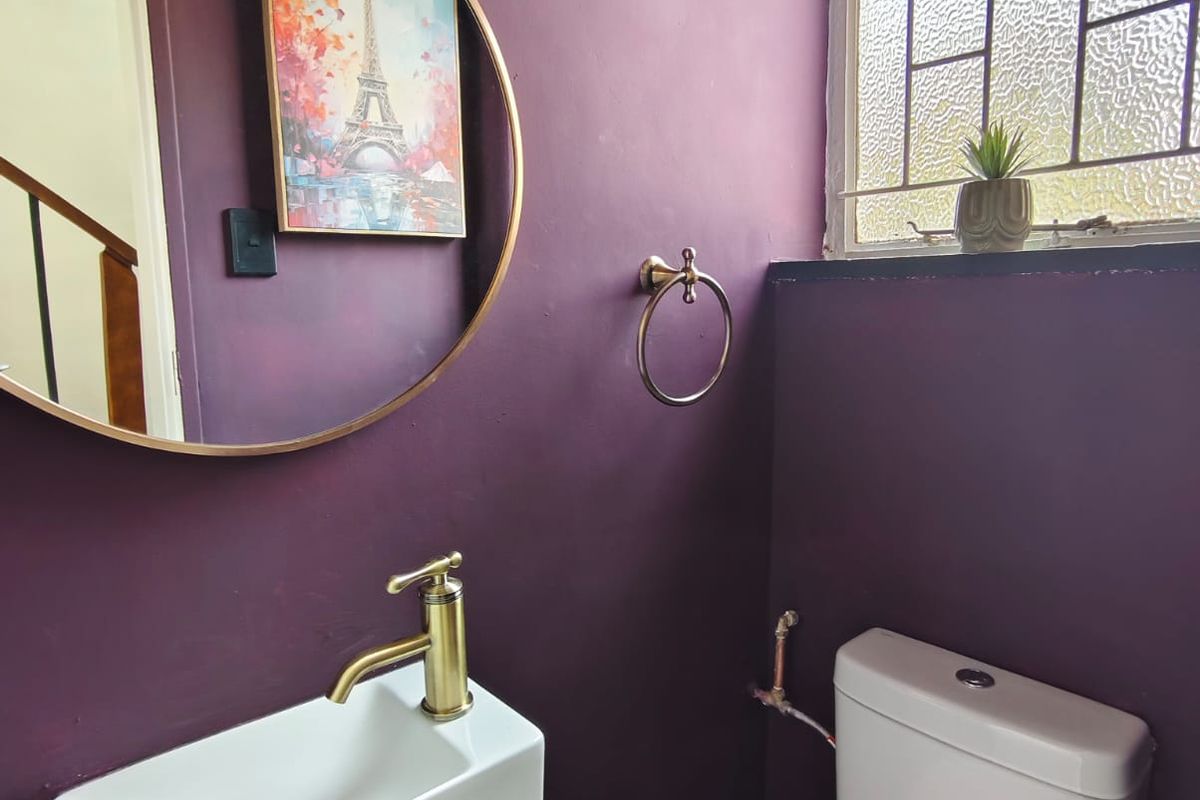 A compact bathroom featuring a wall-mounted basin with brass tapware, a modern toilet, and a window with textured glass.
