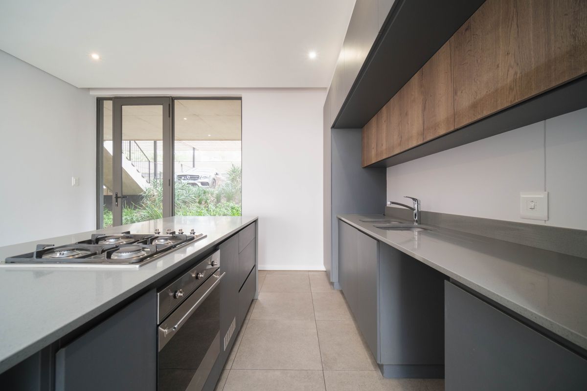 Modern kitchen featuring sleek grey cabinetry, wood-look upper cabinets, stone countertops, a central island with a gas hob, and built-in oven.