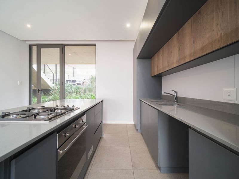 Modern kitchen featuring sleek grey cabinetry, wood-look upper cabinets, stone countertops, a central island with a gas hob, and built-in oven.