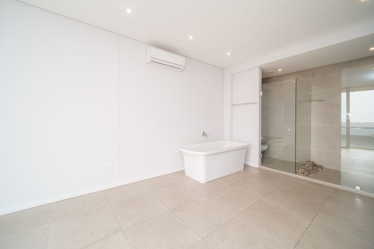 Modern, minimalist bathroom featuring a freestanding bathtub, a spacious glass-enclosed shower with stone pebble flooring, and recessed lighting.