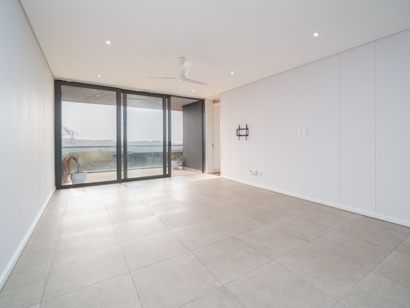 A bright, modern, and spacious living area featuring large sliding glass doors that open onto a balcony, complemented by neutral tiled flooring and recessed lighting.