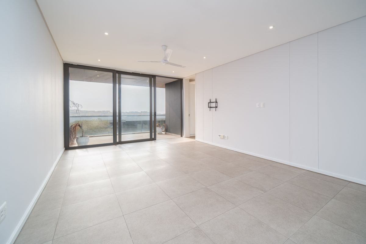 A bright, modern, and spacious living area featuring large sliding glass doors that open onto a balcony, complemented by neutral tiled flooring and recessed lighting.