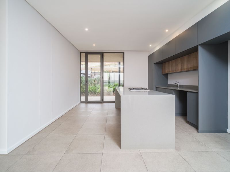 Modern, minimalist kitchen featuring a central island with a gas hob, sleek cabinetry, stone countertops, and direct access to an outdoor area.