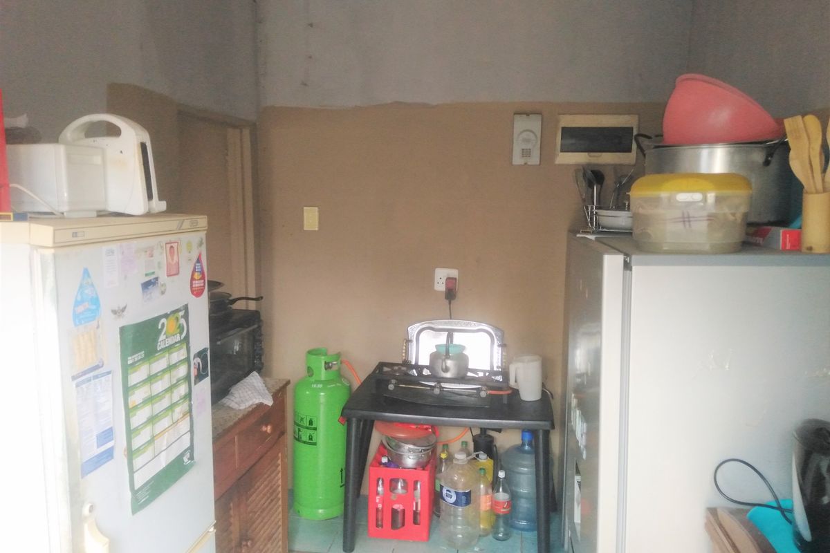 A small, basic kitchen area featuring tiled flooring and plain wall finishes, currently utilized with portable cooking equipment and freestanding appliances.