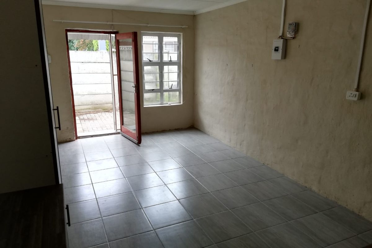 An empty living area featuring tiled flooring, a single window, and a door leading to an exterior paved space.