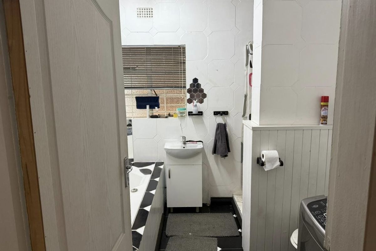 A functional bathroom featuring a vanity basin, bathtub with patterned tiling, and beadboard wall paneling.