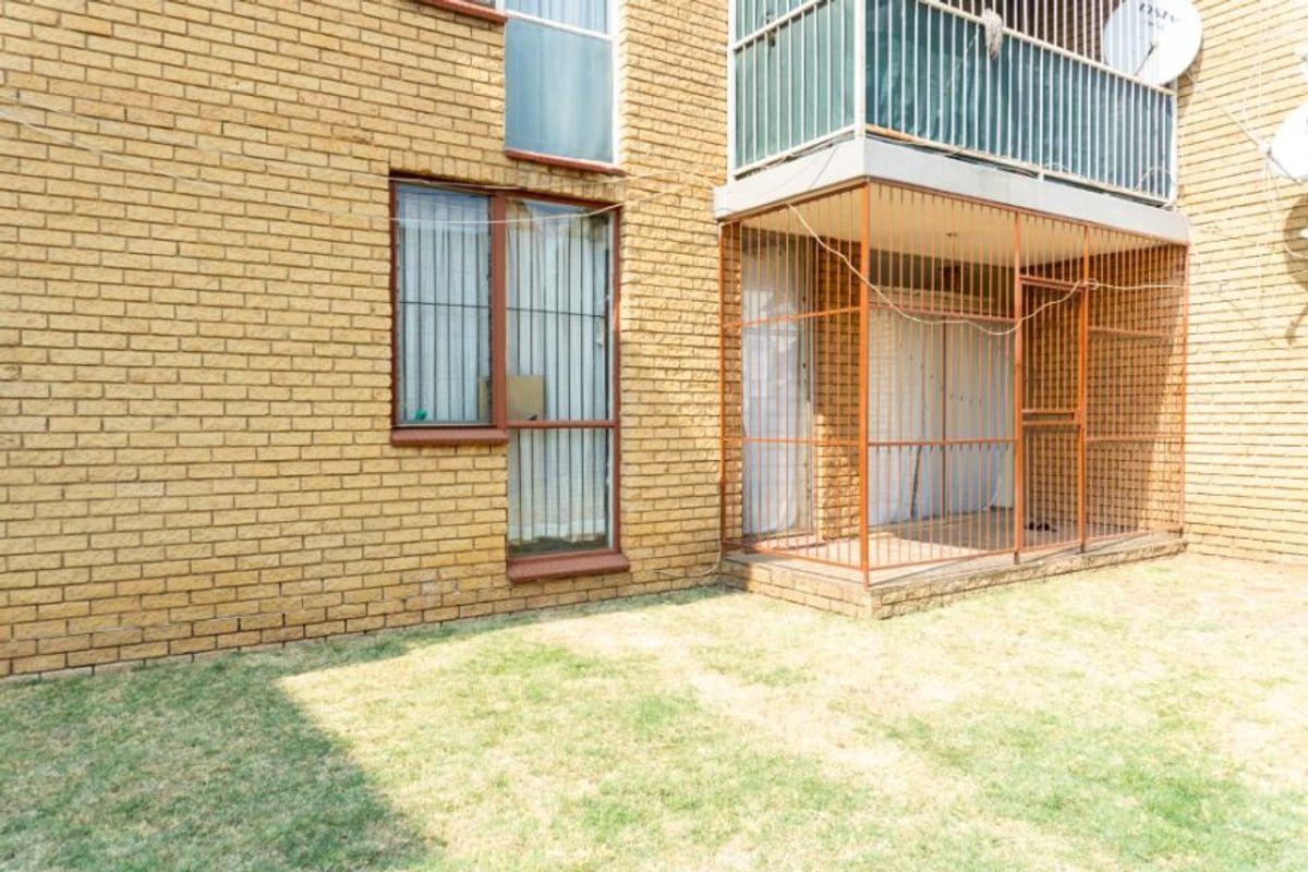 Rear view of the apartment building featuring a brick facade, a ground-level enclosed patio area with security gates, and a small private garden space.