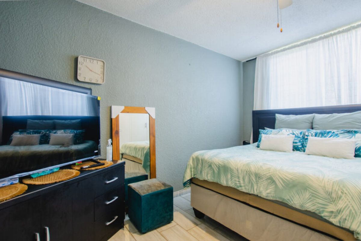 A bedroom featuring tiled flooring, textured walls, and a ceiling fan, providing a functional and comfortable sleeping space.