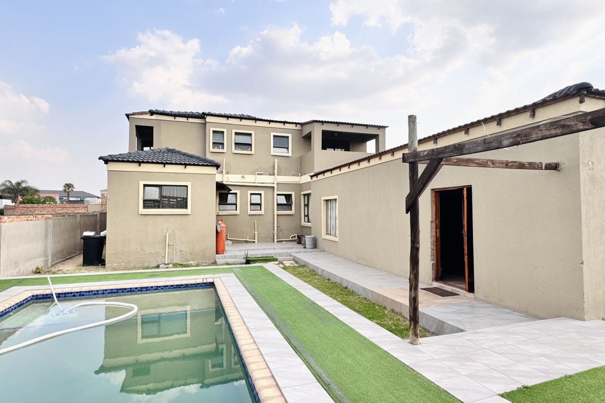 Rear view of the property featuring a swimming pool, tiled patio area, artificial lawn, and a timber pergola structure.