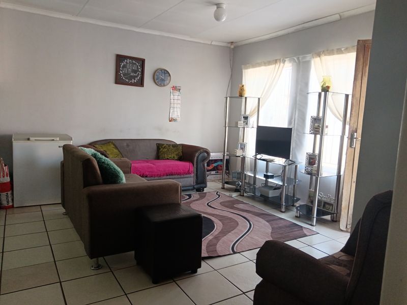 A functional living room featuring tiled flooring and natural light from large windows, providing a comfortable space for relaxation.