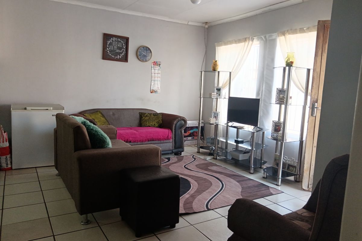 A functional living room featuring tiled flooring and natural light from large windows, providing a comfortable space for relaxation.