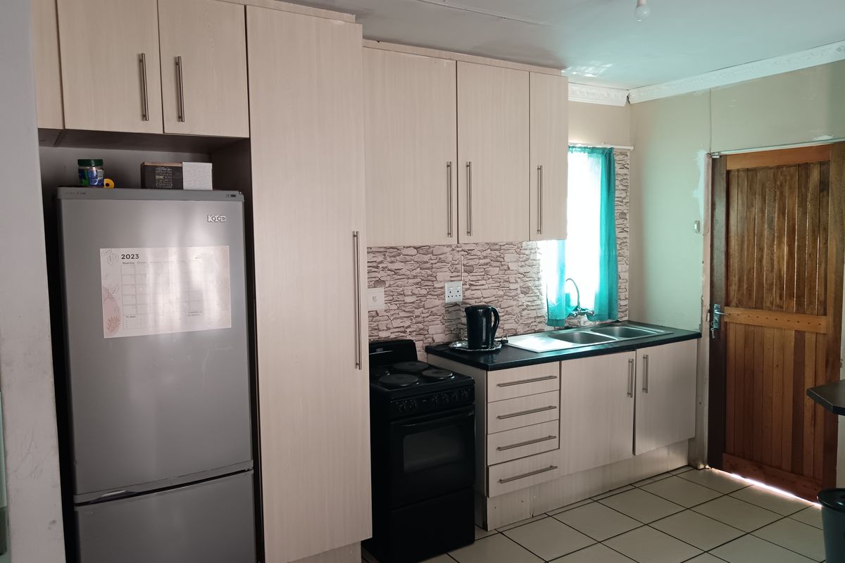 A functional kitchen featuring light-toned cabinetry, a dark countertop, a built-in sink, and a freestanding stove, with direct access to an exterior wooden door.