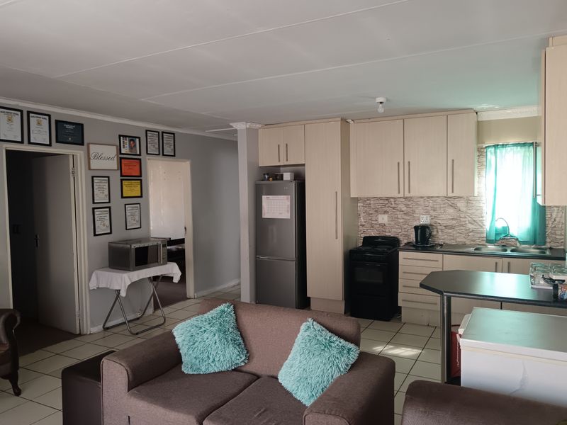 Open-plan living area featuring a functional kitchen with light-toned cabinetry, tiled flooring, and direct access to adjacent rooms.