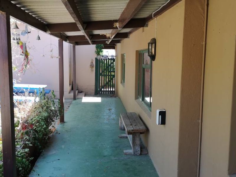 A covered outdoor patio area featuring a painted concrete floor, timber support beams, and access to the rear garden through a wooden gate.