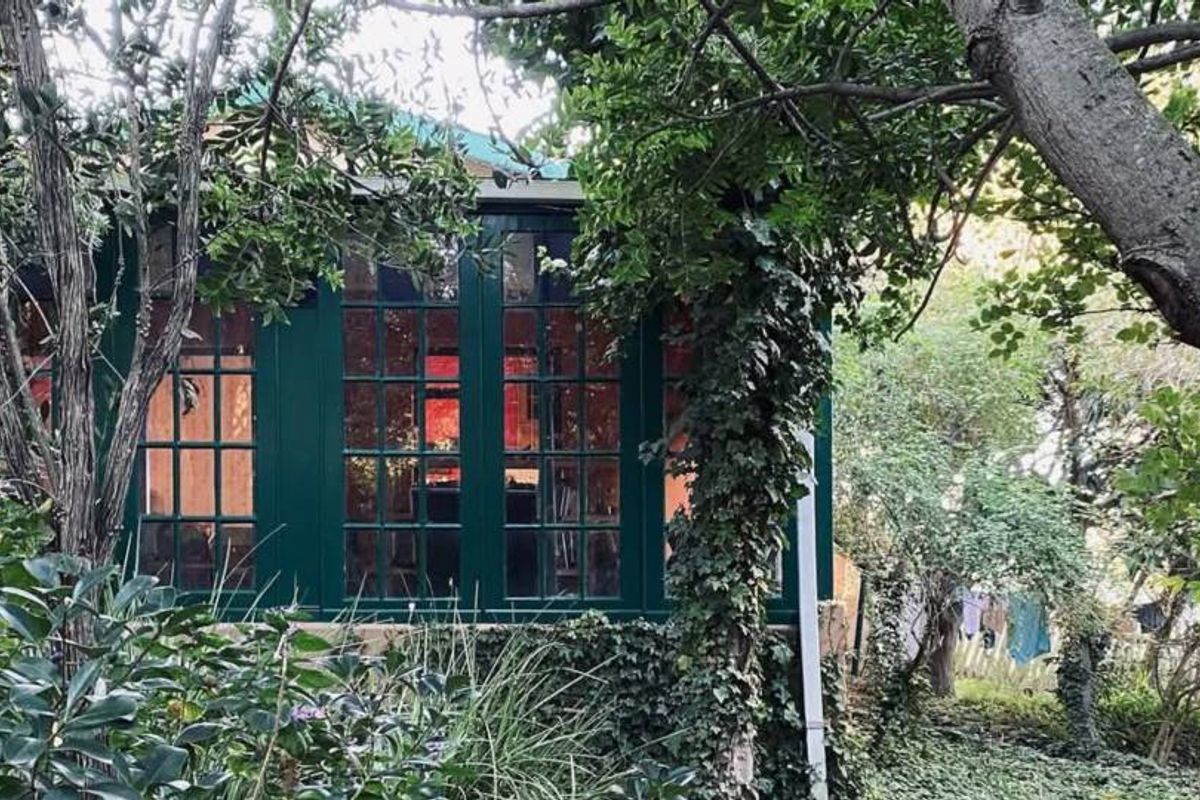 A view of the rear exterior of the property, featuring dark-framed glass windows and doors surrounded by mature trees and garden foliage.
