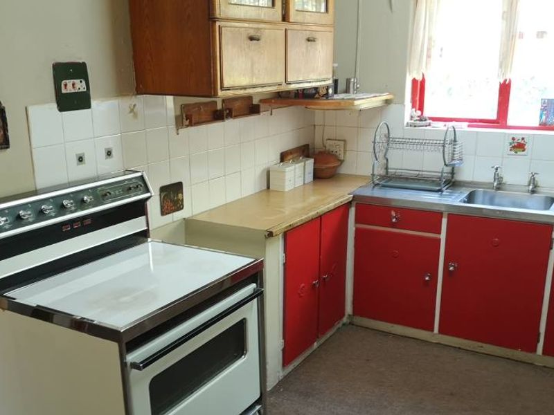 A dated kitchen featuring red cabinetry, a stainless steel sink, and a freestanding stove, offering potential for a modern renovation.