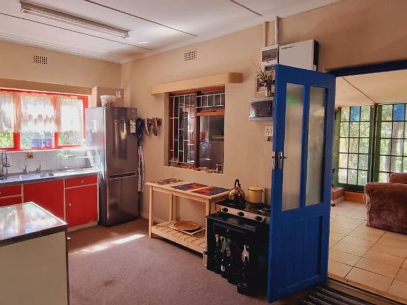 A dated kitchen featuring red cabinetry, a double sink, and direct access to an adjacent sunroom or patio area.