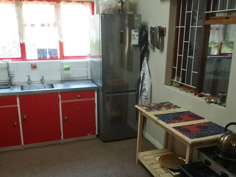 A functional kitchen featuring red cabinetry, a stainless steel sink, and large windows providing natural light.