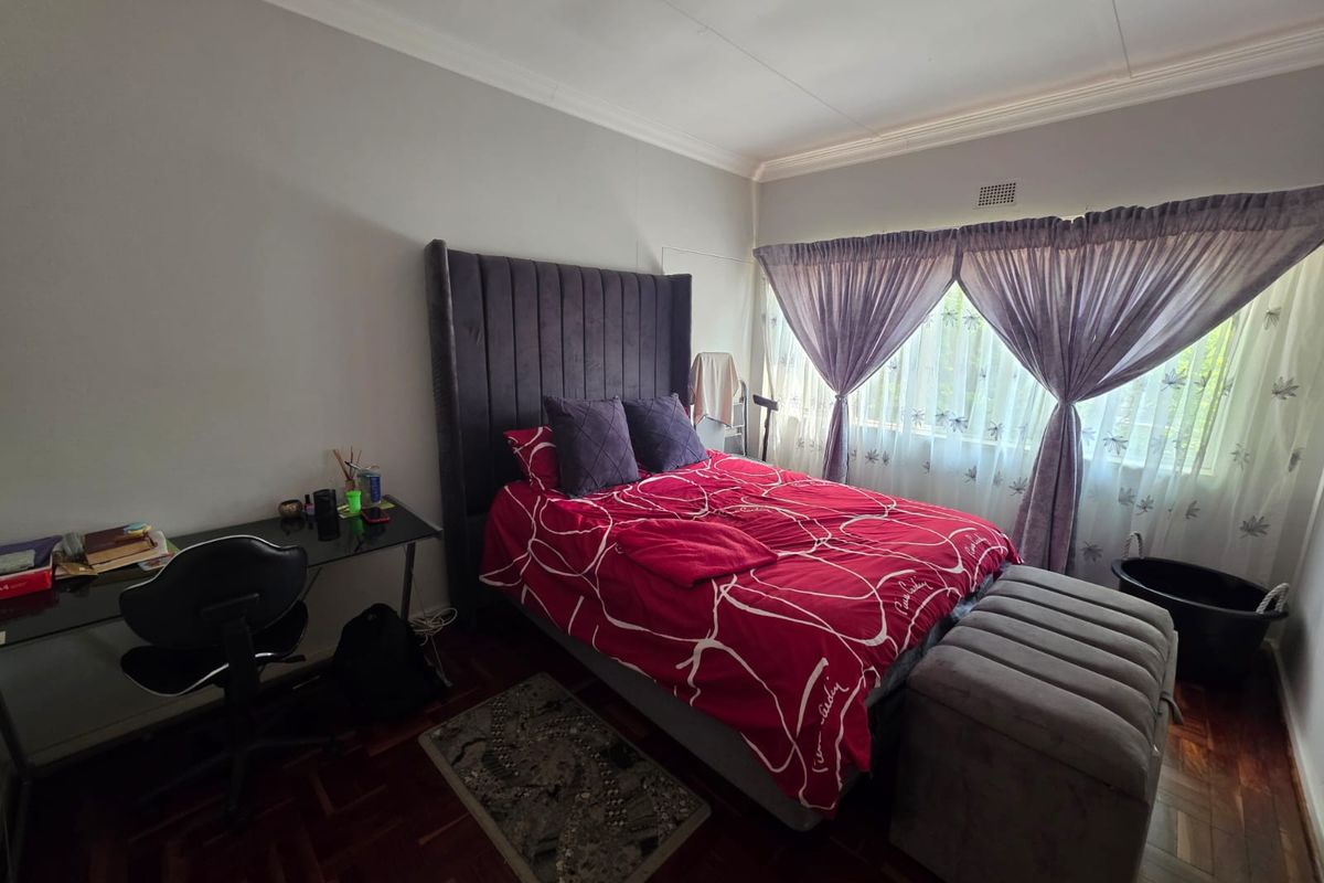 A bedroom featuring classic parquet flooring, crown molding, and large windows with curtains, providing a functional and well-lit living space.