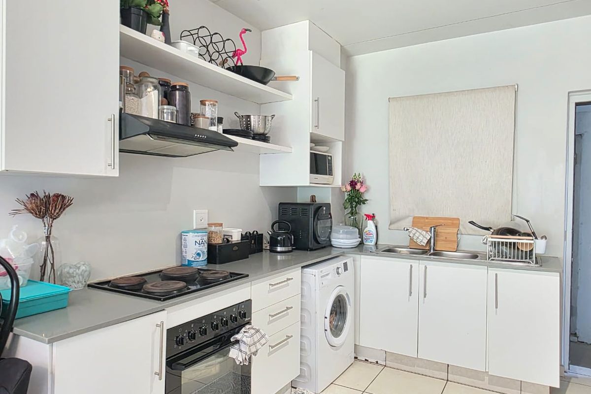 Functional kitchen featuring white cabinetry, integrated oven and hob, extractor fan, stainless steel sink, and space for a front-loading washing machine.