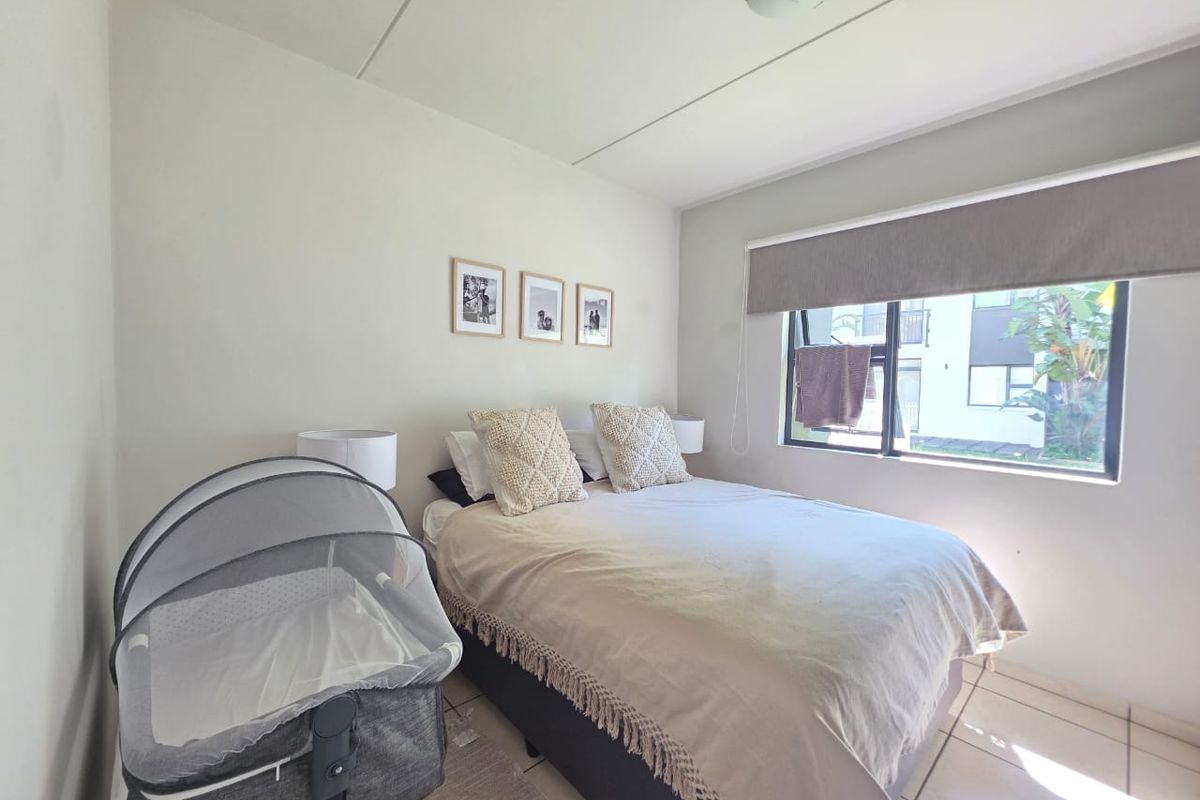 A well-lit bedroom featuring tiled flooring, a large window with a roller blind, and a neutral color palette.
