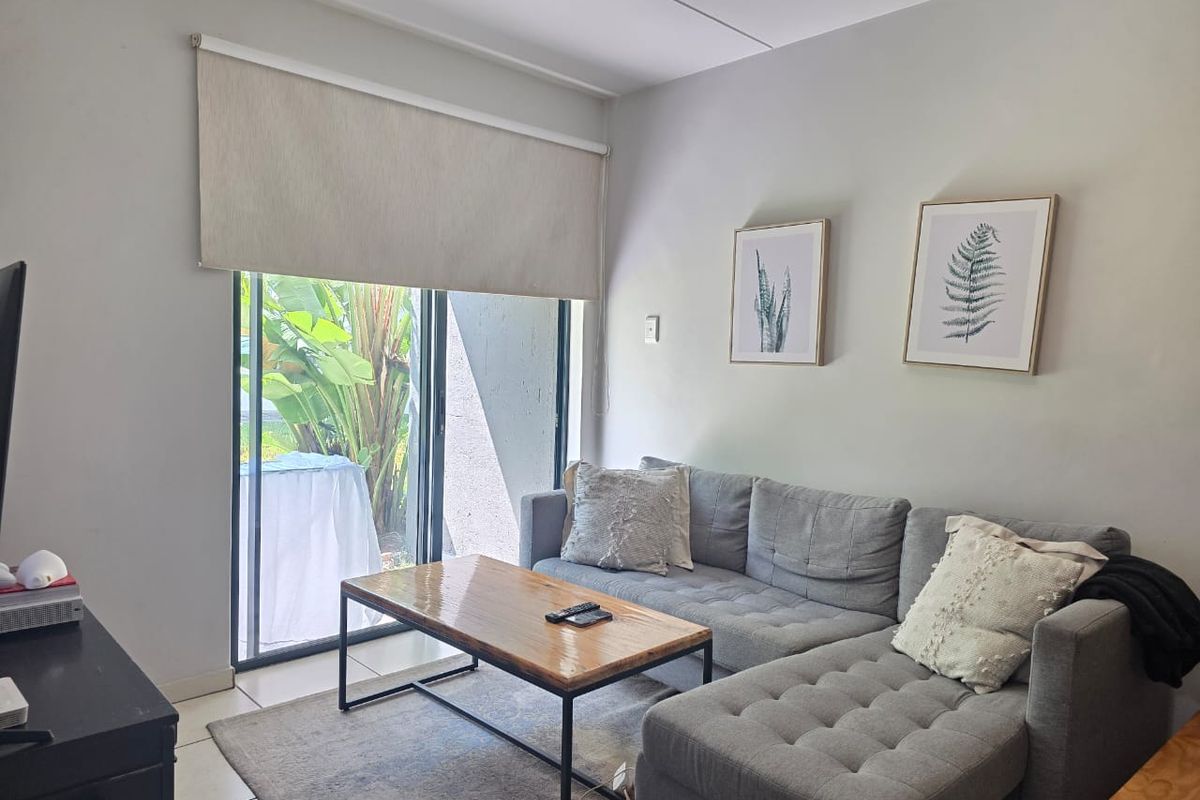 A comfortable living room featuring tiled flooring, a large sliding glass door with a roller blind, and direct access to an outdoor patio area.