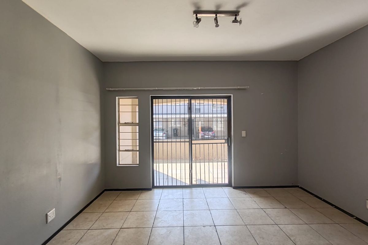 An empty living room featuring neutral grey walls, tiled flooring, and a security gate leading to an outdoor area.