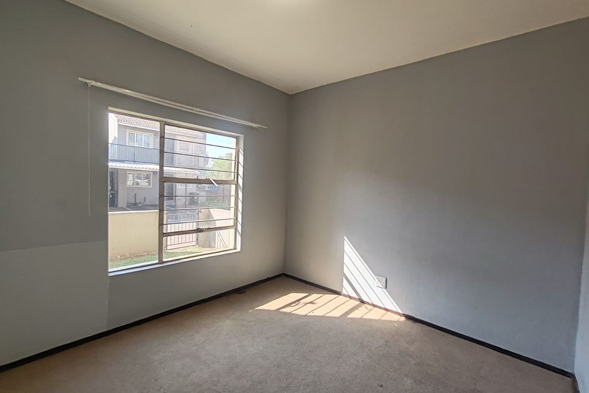 A vacant bedroom featuring neutral grey walls, carpeted flooring, and a large window with security bars, offering a blank canvas for personalization.