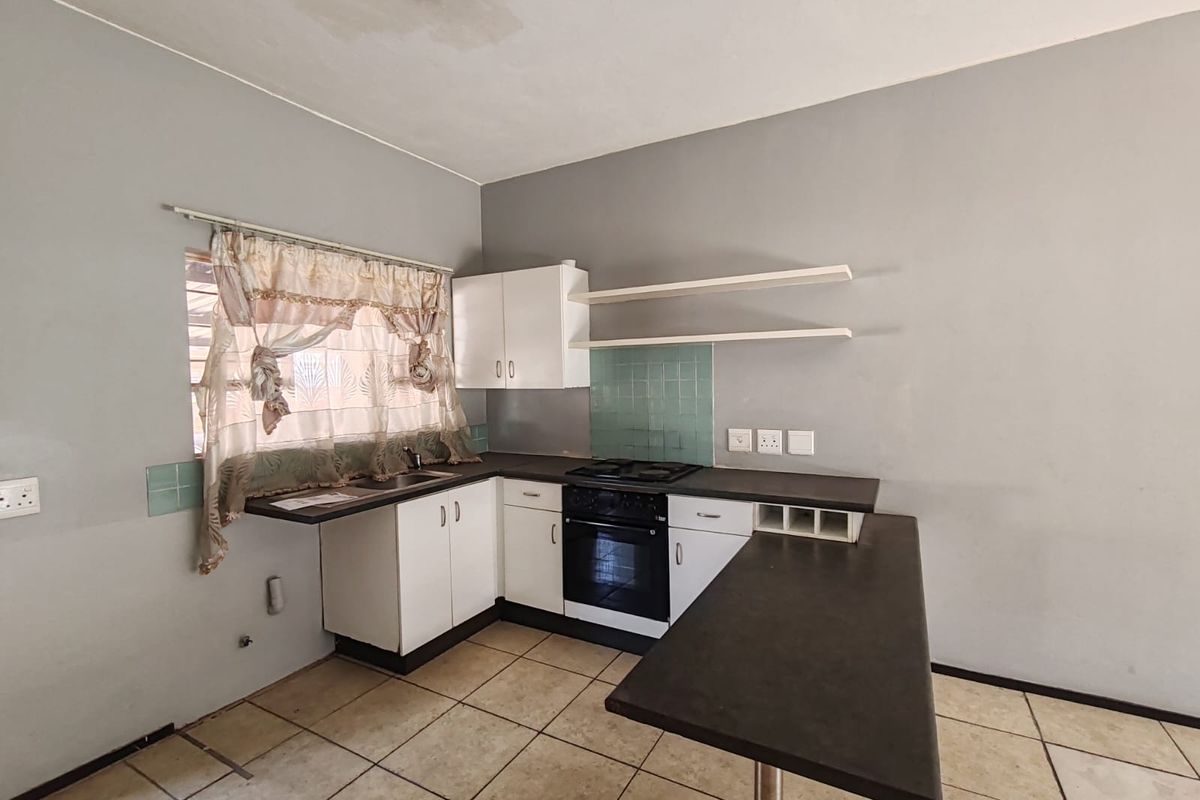 A compact kitchen featuring white cabinetry, a built-in oven with hob, dark countertops, and tiled flooring, requiring some cosmetic updates.
