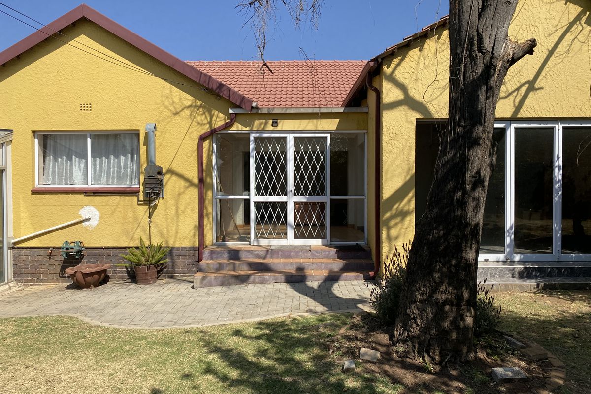 Rear view of the house featuring a paved patio area, security gate entrance, and textured yellow exterior walls with tiled roofing.