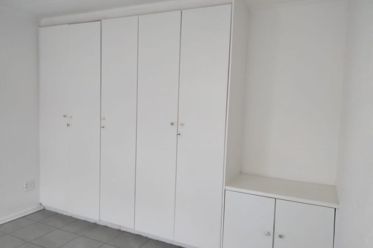 A clean, empty bedroom featuring white built-in cupboards with integrated storage shelving and neutral tiled flooring.