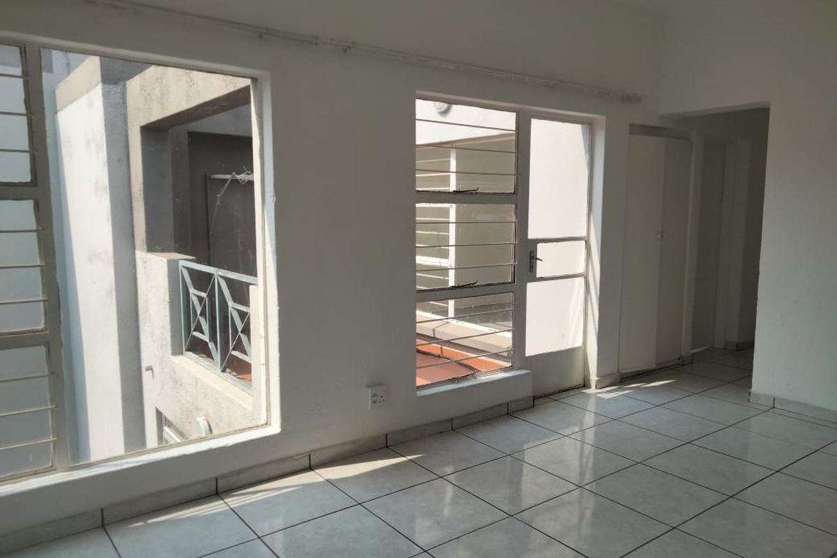 An empty living area featuring tiled flooring, large windows with security bars, and access to an outdoor balcony area.