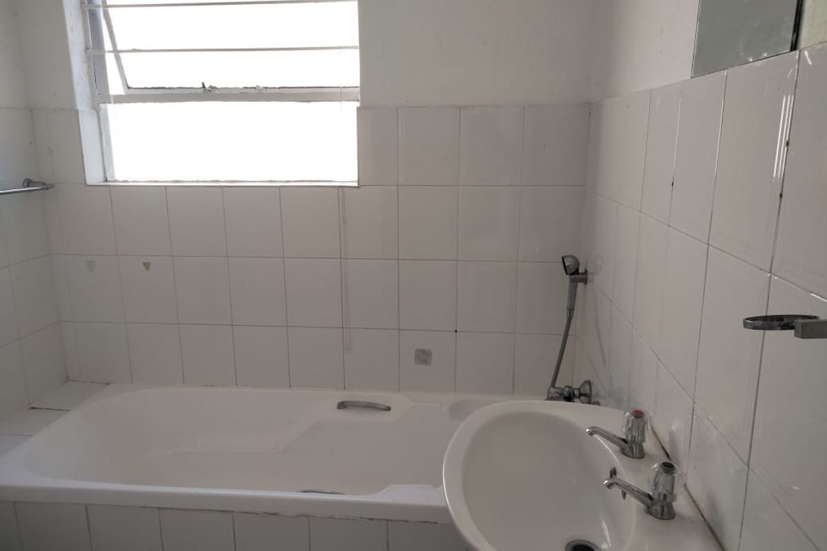 A dated bathroom featuring a standard bathtub, wall-mounted basin, and tiled walls, requiring renovation to update the finishes and fixtures.