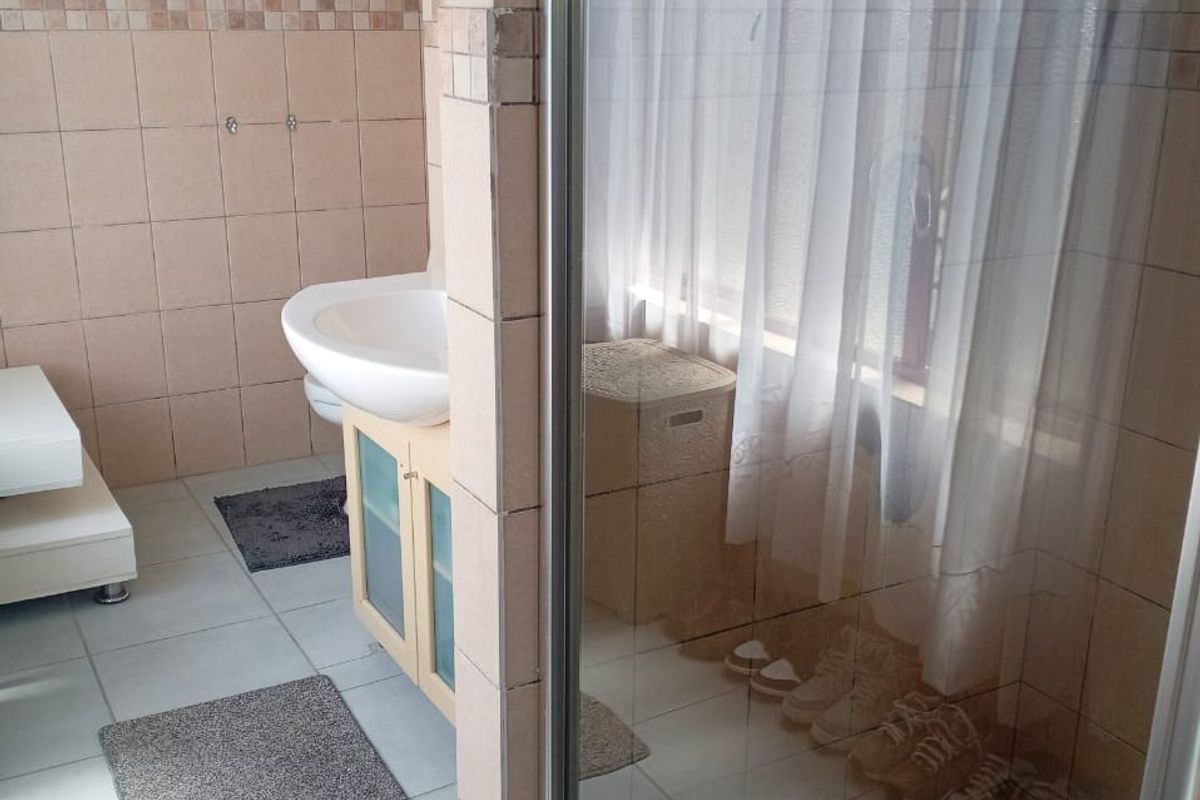 A functional bathroom featuring a vanity basin, tiled walls, and a glass-enclosed shower area with mosaic floor detailing.