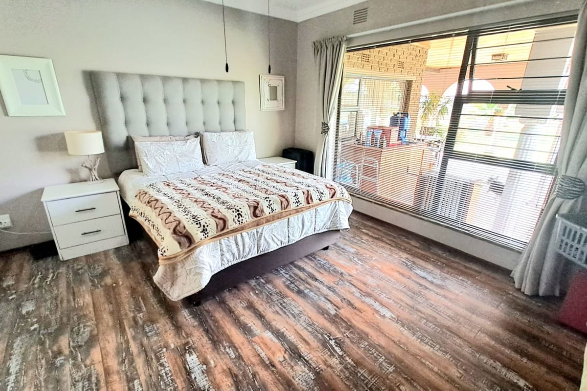 A well-lit bedroom featuring wood-look laminate flooring, a large window with blinds, and a neutral color palette.