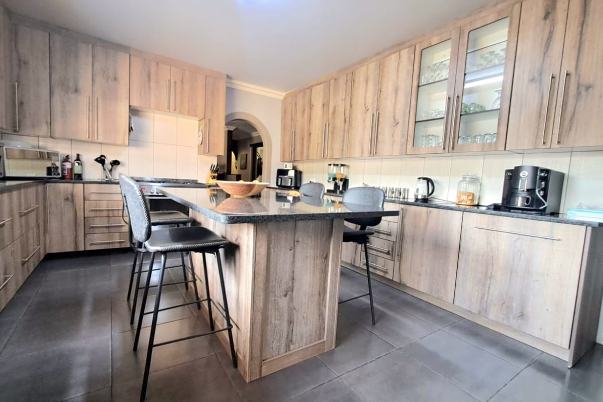Modern kitchen featuring wood-grain cabinetry, a central island with stone countertop, and tiled flooring, offering a functional and contemporary cooking space.
