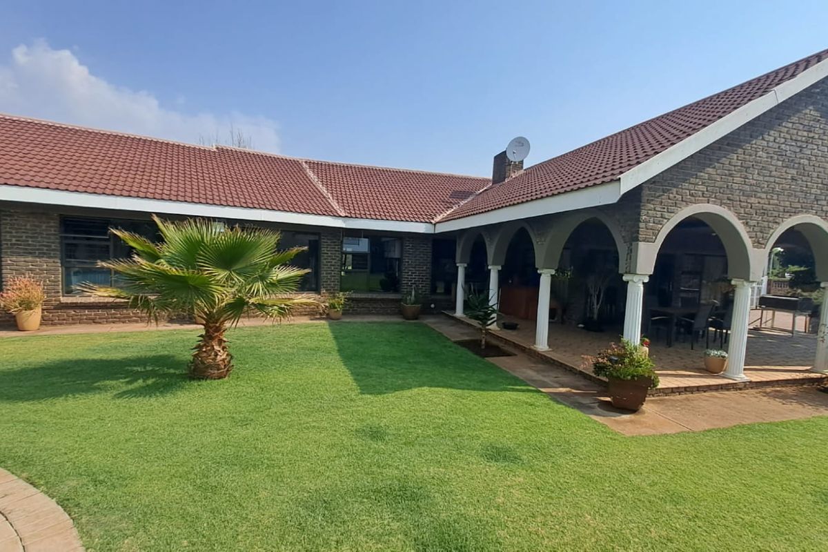 A spacious rear garden featuring a well-maintained lawn and a covered patio area with arched columns, ideal for outdoor entertaining.