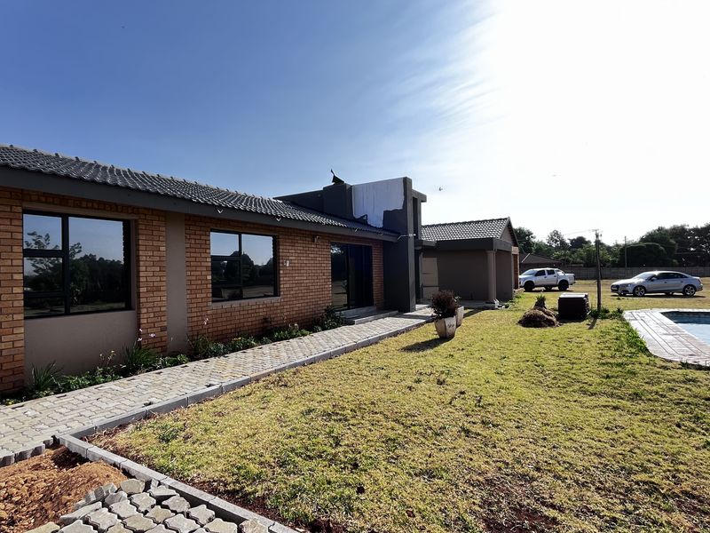 Rear view of the property featuring a brick and plaster facade, paved walkway, lawn, and an outdoor swimming pool.