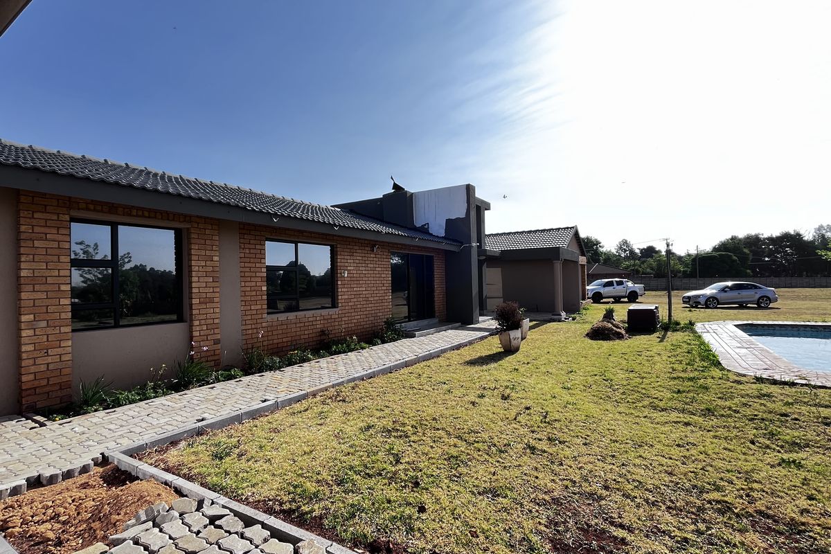 Rear view of the property featuring a brick and plaster facade, paved walkway, lawn, and an outdoor swimming pool.