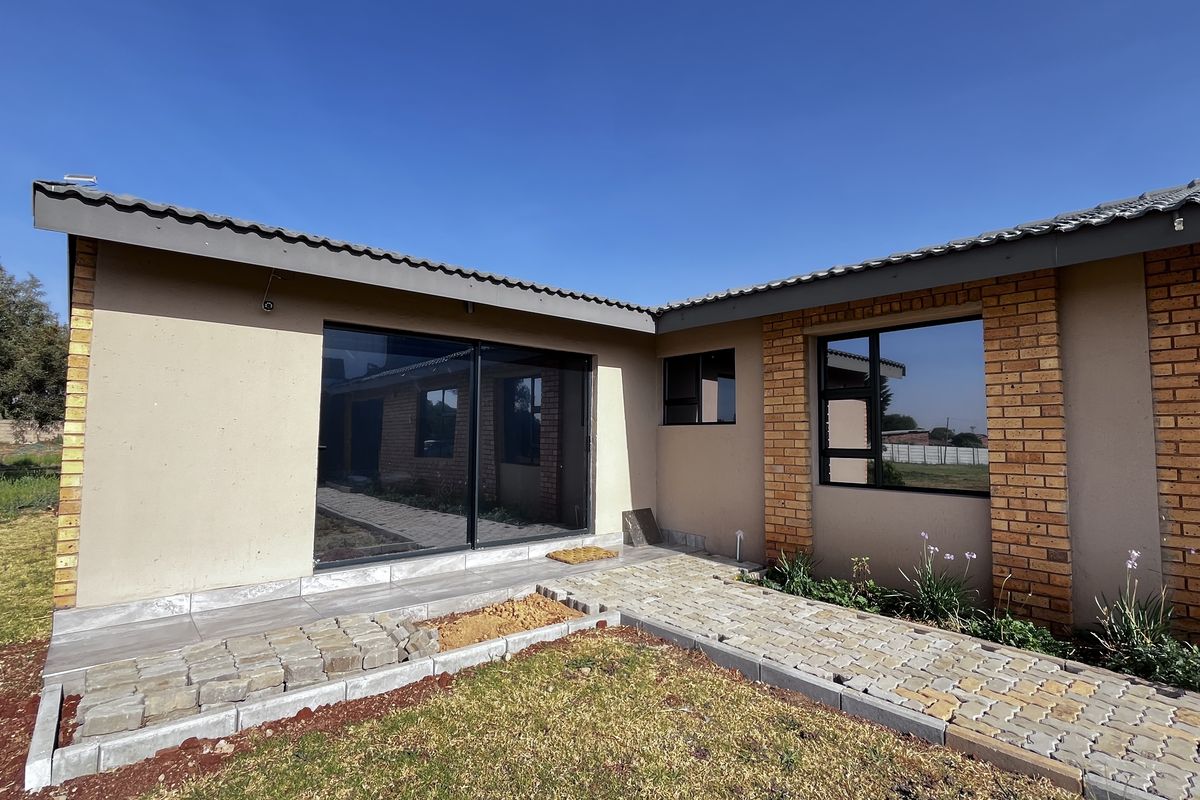 Rear exterior view of the property featuring a paved walkway, sliding glass doors, and brick-accented facade with a tiled roof.