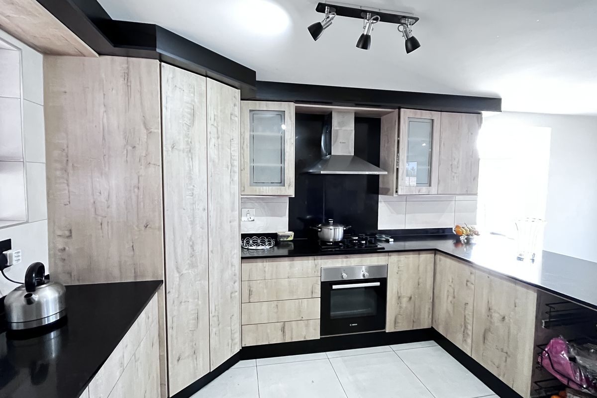 Modern kitchen featuring light wood-grain cabinetry, contrasting black countertops, a built-in oven, gas hob, and stainless steel extractor fan.