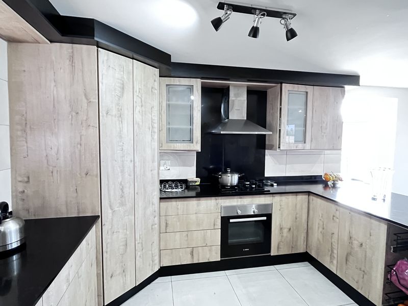 Modern kitchen featuring light wood-grain cabinetry, contrasting black countertops, a built-in oven, gas hob, and stainless steel extractor fan.