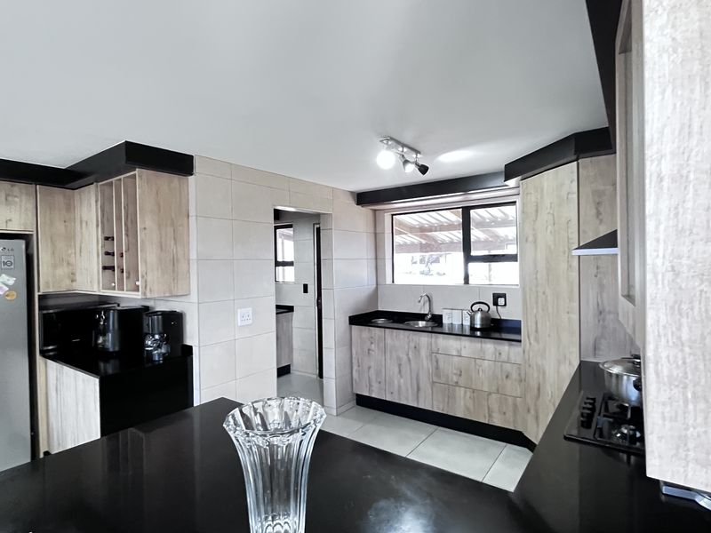 Modern kitchen featuring light wood-grain cabinetry, contrasting black granite countertops, tiled splashbacks, and a functional layout with an adjacent scullery area.