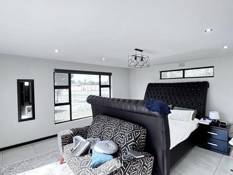 Spacious bedroom featuring modern tiled flooring, recessed downlighting, a contemporary pendant light fixture, and large windows providing ample natural light.